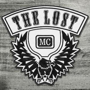 May include: A black and white embroidered patch featuring an arched top banner with the text THE LOST in a bold font. Below the banner is a central shield containing the letters MC, flanked by a large eagle with spread wings in black thread.