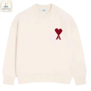 May include: A cream-colored long-sleeve sweater with a crew neckline and ribbed cuffs and hem. The chest features a red embroidered heart logo with the letter A integrated at the base. The interior neck label displays the text ami.