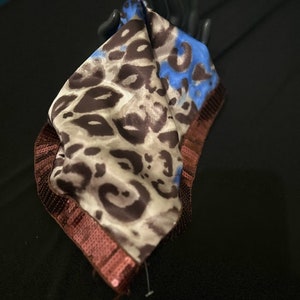 Puede incluir: Un pañuelo de seda con estampado de leopardo marrón y beige con ribete de lentejuelas azules y marrones.