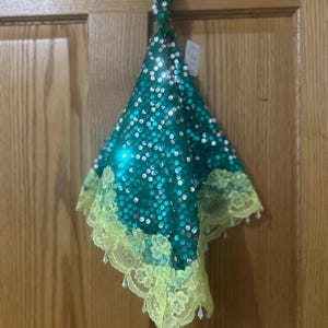 May include: A teal sequined accessory with a yellow lace trim and hanging beads. The item is hanging on a wooden door. The sequins are round and reflective. The lace trim has a floral pattern.
