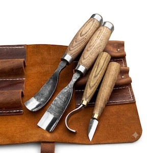 May include: A set of four woodworking carving tools with light brown wood handles and metal ferrules, featuring varied blade shapes including curved and straight edges, resting on a brown leather tool roll with stitched pockets and metal rivets.
