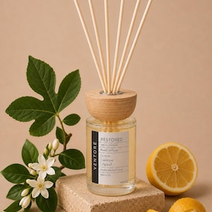 May include: A clear glass reed diffuser bottle with a light wood cap and five reeds. The label reads VENTORE RESTORED 100 ml/3.4 fl.oz Reed diffuser citrus jasmine fig leaf Handcrafted in Oxford Batch 001. Accompanied by white jasmine flowers and a lemon.