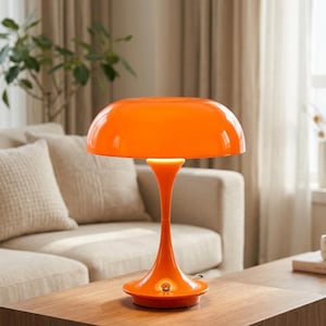 Peut inclure: Une lampe de table orange vif dotée d'un large abat-jour en forme de dôme et d'un pied élancé et incurvé. La lampe présente une finition brillante et un petit interrupteur circulaire situé sur l'avant du socle, diffusant une lumière douce.