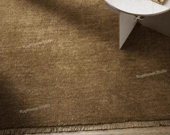 May include: A solid brown area rug with a textured, woven surface and a short fringe along the bottom edge. The rug features a consistent earthy tone and a dense pile construction, providing a uniform appearance across the entire visible surface area.