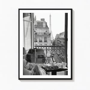 Könnte beinhalten: Ein schwarz-weiß gerahmter Wandkunstdruck, der eine Person im weißen Bademantel zeigt, die auf einem Balkon die Zeitung Le Figaro liest. Ein Frühstücksset mit Teekanne und Tassen steht auf einem Tisch, mit Blick auf Pariser Gebäude und den Eiffelturm.