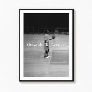 May include: A black and white framed wall art print featuring a basketball player standing on a court holding a ball. The text Outwork Everyone is printed in white across the center. The player wears a t-shirt and plaid pants on the court.