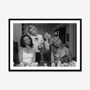 May include: A black and white framed photograph featuring four individuals in an indoor setting. One person wears a graphic t-shirt, while others wear tank tops. The composition captures a group of friends in a casual, domestic environment.