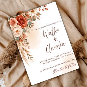 May include: A rectangular wedding invitation card featuring a floral arrangement of rust-colored roses, cream flowers, and dried pampas grass. The text reads: YOU ARE INVITED TO THE WEDDING OF Watter & Claudia, SATURDAY, OCTOBER 15TH, 2030, 321 BLOSSOM COURT, HAVENWOOD, Reception to follow!
