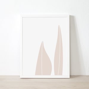 Puede incluir: Una impresión artística enmarcada con un diseño minimalista. Dos formas abstractas de hojas en un color beige apagado sobre un fondo blanco. La obra de arte está encerrada en un marco blanco, adecuada para la decoración del hogar.