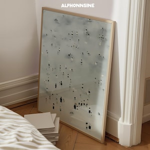 Puede incluir: Una impresión artística enmarcada que representa una escena de playa con numerosas figuras pequeñas en blanco y negro. La obra de arte se muestra en un marco de madera clara y se apoya contra una pared. El texto "ALPHONNSINE" está en la parte superior.