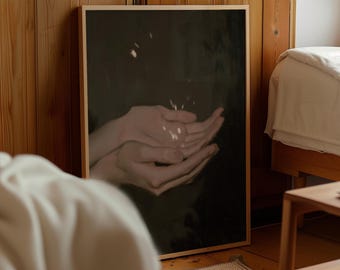 May include: A rectangular wall art print in a light wood frame featuring a dark, moody painting of two cupped hands held together. The hands are illuminated by soft, scattered light highlights against a deep, dark, and indistinct background.