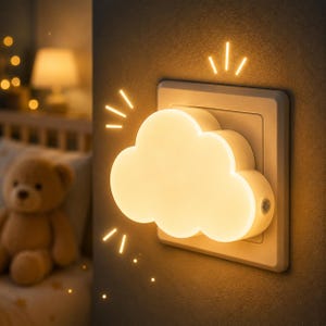 Può includere: Una luce notturna a forma di nuvola inserita in una presa a muro che emette un bagliore caldo e soffuso. Il dispositivo in plastica bianca è montato direttamente sulla presa e presenta un piccolo sensore circolare sul lato del corpo.