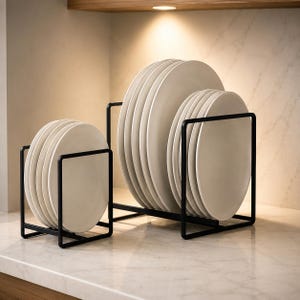 May include: Two black metal wire plate racks holding stacks of round, off-white ceramic plates. The smaller rack on the left holds four plates, while the larger rack on the right holds six plates, all arranged vertically in a clean, organized display.
