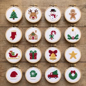 May include: Sixteen circular wooden embroidery hoops containing individual cross-stitch designs of Christmas icons including a tree, reindeer, snowman, gingerbread man, stocking, house, candy cane, candle, sleigh, gift, bell, star, hat, mitten, truck, and wreath.