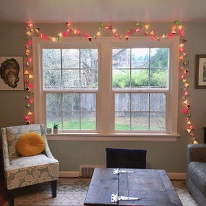 May include: A living room with a large window featuring a string of colorful triangle lights. The lights are strung across the top of the window and hang down the side. There is a couch and a coffee table in the room.