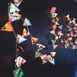 May include: A string of colorful paper triangle lights, hanging from a dark wall. The triangles are made of paper and have different patterns and colors, including green, blue, yellow, and red.