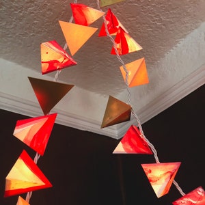 May include: A string of triangle-shaped lights with a marbled red and white design. The lights are strung together with white wire and are hanging from a white ceiling.