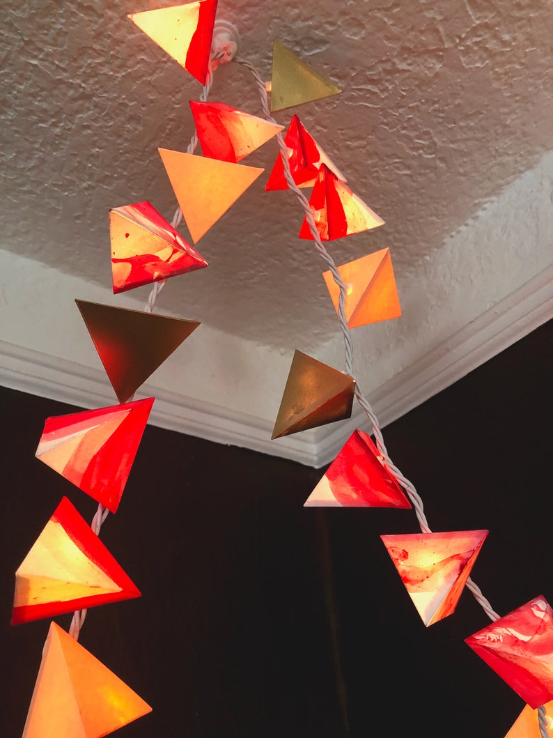 May include: A string of triangle-shaped lights with a marbled red and white design. The lights are strung together with white wire and are hanging from a white ceiling.