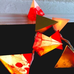 May include: A string of pyramid-shaped lights with a red, gold, and orange color scheme. The lights are made of paper and have a watercolor-like design.