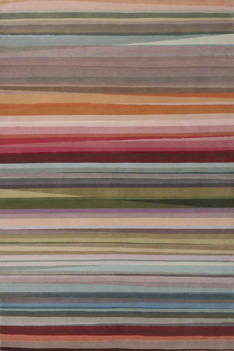 May include: A rectangular area rug featuring a series of horizontal stripes in varying widths and colors, including shades of muted red, orange, pink, olive green, light blue, grey, and beige, creating a layered, multi-toned linear pattern.