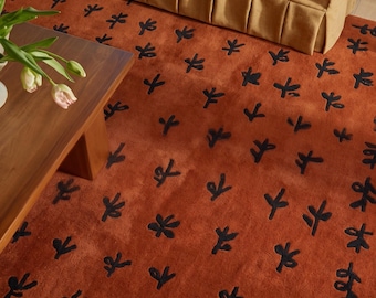 May include: A rectangular area rug featuring a deep burnt orange background with a repeating pattern of small, black, hand-drawn style floral motifs scattered across the surface in a grid-like arrangement.