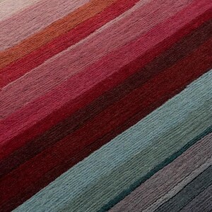 May include: A textile surface featuring a series of diagonal stripes in a gradient of colors. The pattern transitions from warm tones of orange, pink, and deep red to cooler shades of teal, blue, and dark gray, creating a textured, linear design.