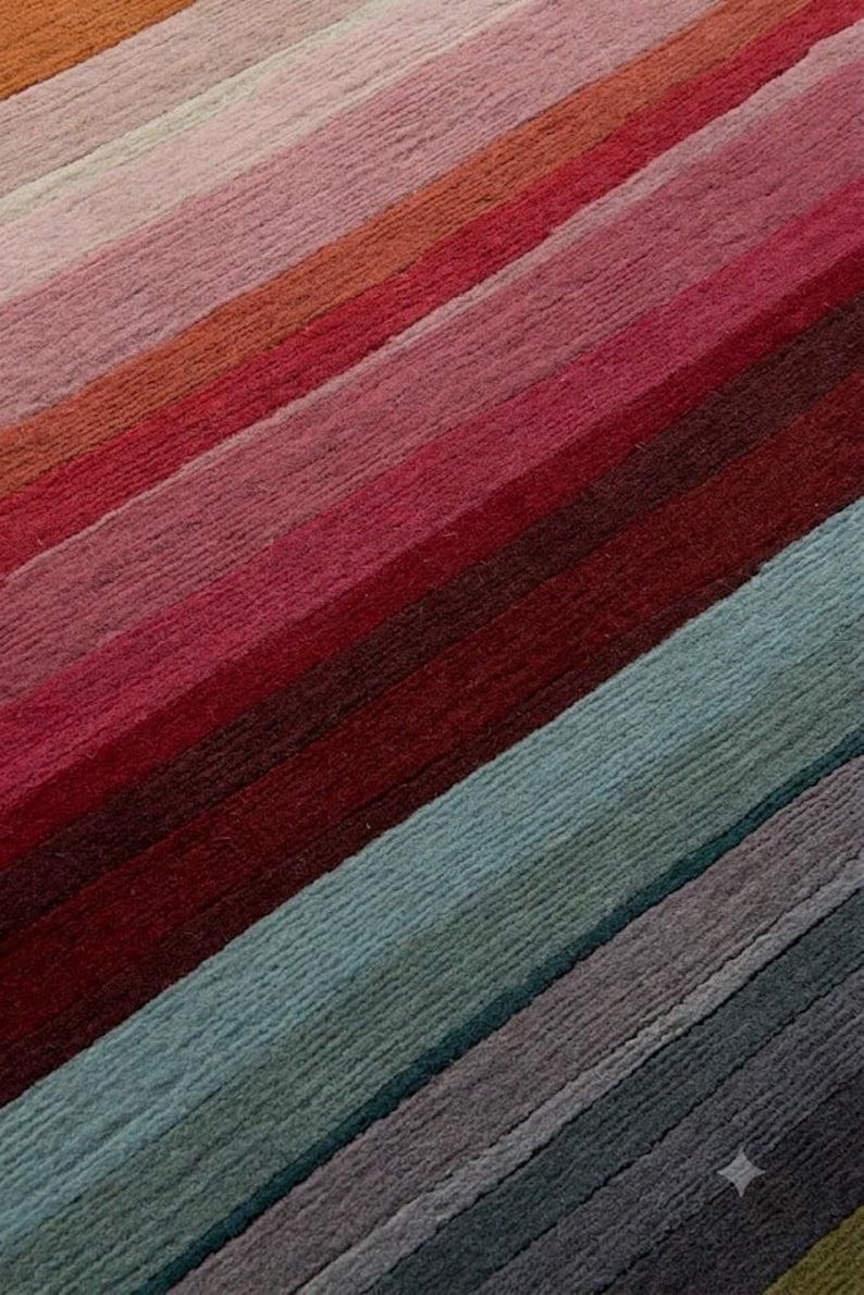 May include: A textile surface featuring a series of diagonal stripes in a gradient of colors. The pattern transitions from warm tones of orange, pink, and deep red to cooler shades of teal, blue, and dark gray, creating a textured, linear design.