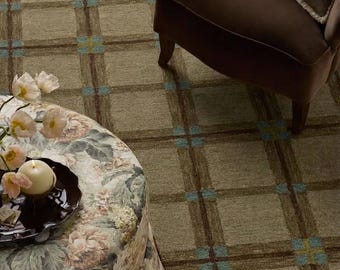 May include: A round floral ottoman with a pleated skirt, topped with a black tray, a white candle, and pale flowers. Beside it sits a brown armchair with a floral pillow, all placed on a tan rug featuring a brown and blue plaid grid pattern.