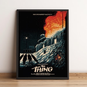 Op de afbeelding: Een ingelijste filmposter voor John Carpenter's The Thing met een donker, besneeuwd landschap en een groot oranje vuur dat uit een gebouw komt. De tekst luidt MAN IS THE WARMEST PLACE TO HIDE en THE THING met extra kleine credits onderaan.