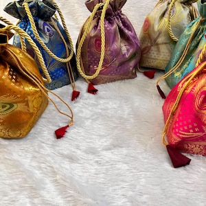 May include: A collection of six drawstring pouches in various colors including gold, blue, purple, and pink. Each pouch features a repeating peacock feather pattern, a metallic sheen, gold braided drawstrings, and small dark red fabric tassels.