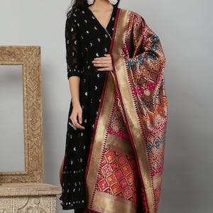 May include: A black V-neck kurta with gold-toned patterns, paired with black trousers and a multicoloured dupatta featuring intricate geometric designs, a wide gold border, and dark red tassels along the hemline, worn with silver-toned jewellery.
