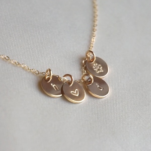 Może przedstawiać: Złoty naszyjnik z pięcioma zawieszkami, w tym sercem, odciskiem łapy i trzema zawieszkami z inicjałami.