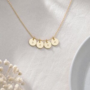 Op de afbeelding: Een goudkleurige ketting met een fijne schakelketting en vier kleine, ronde hangers. Elke hanger is gegraveerd met een hoofdletter, die van links naar rechts de reeks G, C, G en M vormen. Het metaal heeft een gepolijste afwerking.