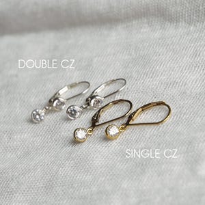 May include: Two pairs of silver earrings with clear cubic zirconia stones. The top pair has two stones on each earring, while the bottom pair has one stone on each earring. The text "DOUBLE CZ" is above the top pair and "SINGLE CZ" is below the bottom pair.