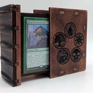 Peut inclure: Une boîte de jeu en bois brun foncé avec un couvercle coulissant gravé de cinq symboles de mana circulaires. La boîte contient une carte à collectionner à bordure verte avec le texte Férox de Fléaudhache et l'illustration d'une créature.