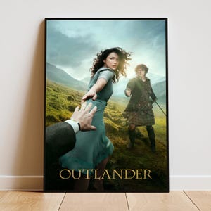 Puede incluir: Un póster enmarcado con una escena de Outlander. Una persona con manga gris extiende la mano hacia una mujer con vestido verde azulado, mientras un hombre con chaqueta verde y falda escocesa está cerca. El fondo muestra un paisaje verde y montañoso.