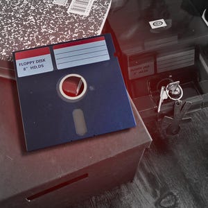 May include: A square blue 8-inch floppy disk with a red label area and white text reading FLOPPY DISK 8" HD,DS. The disk features a central circular hub and a rectangular slot. It is positioned near a black storage box with a key and a notebook.