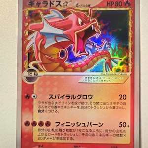 May include: A Japanese Pokémon trading card featuring a red Gyarados with a Delta Species symbol. The card displays 80 HP, the name Gyarados, and two attacks: Spiral Grow and Finish Burn. The artwork is holographic with a fiery orange background.