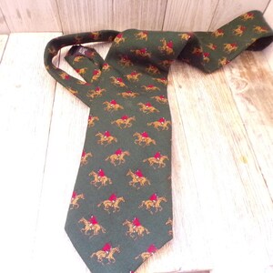 May include: A green silk tie with a repeating pattern of brown horses and riders in red jackets.