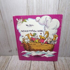 May include: A pink book cover with the title "Tele-Story presents NOAH and the ARK" in white text. The cover features an illustration of Noah's Ark with animals on board, including a camel, giraffe, elephant, and birds. The text "SUPERSCOPE PRODUCTION" is printed in white at the bottom of the cover.