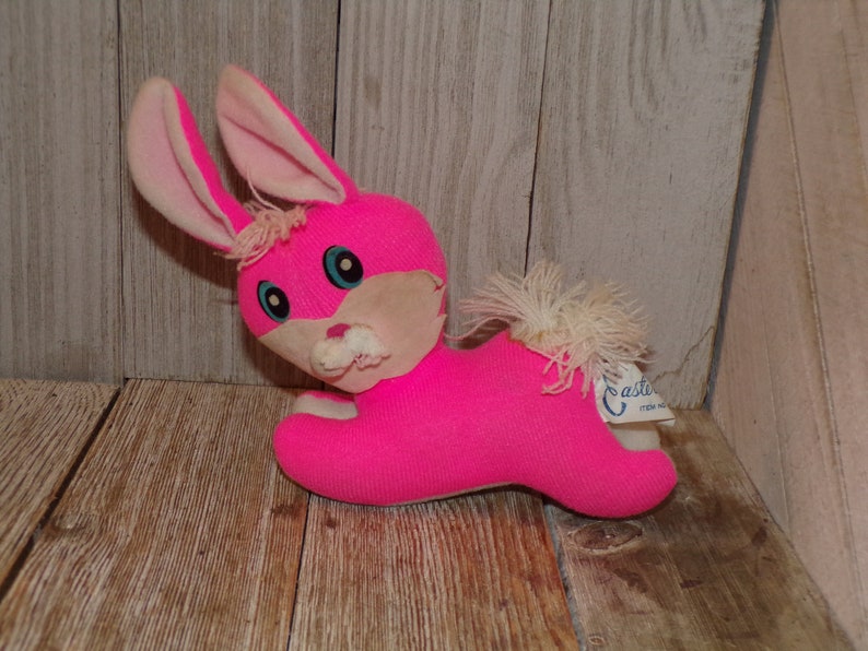 May include: Pink plush bunny rabbit toy with white fur accents and blue eyes. The toy has a white tag that says "Easter" on it.