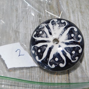 K&ouml;nnte beinhalten: Ein runder Keramikknopf mit einem wei&szlig;en und schwarzen Blumendesign. Der Knopf hat ein Loch in der Mitte.