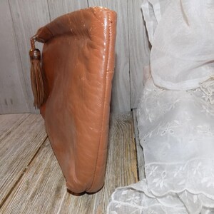 May include: A brown leather clutch with a tassel. The clutch has a flap closure and a smooth, textured surface.