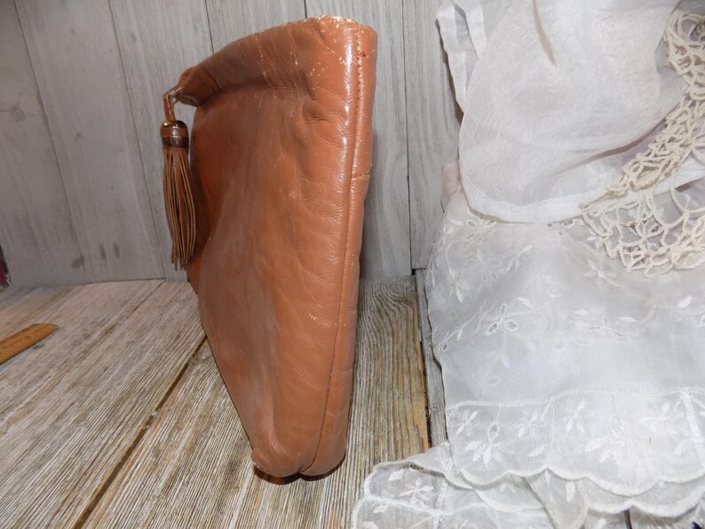 May include: A brown leather clutch with a tassel. The clutch has a flap closure and a smooth, textured surface.