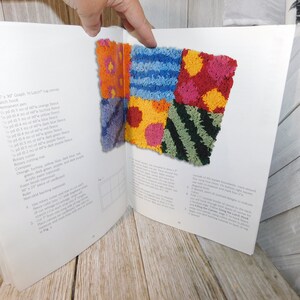 May include: A book open to a page showing instructions for a latch hook rug project. The rug is made of colorful squares of different textures and patterns, including stripes, polka dots, and zigzags. The page also lists the materials needed for the project, including yarn, latch hook, and canvas.