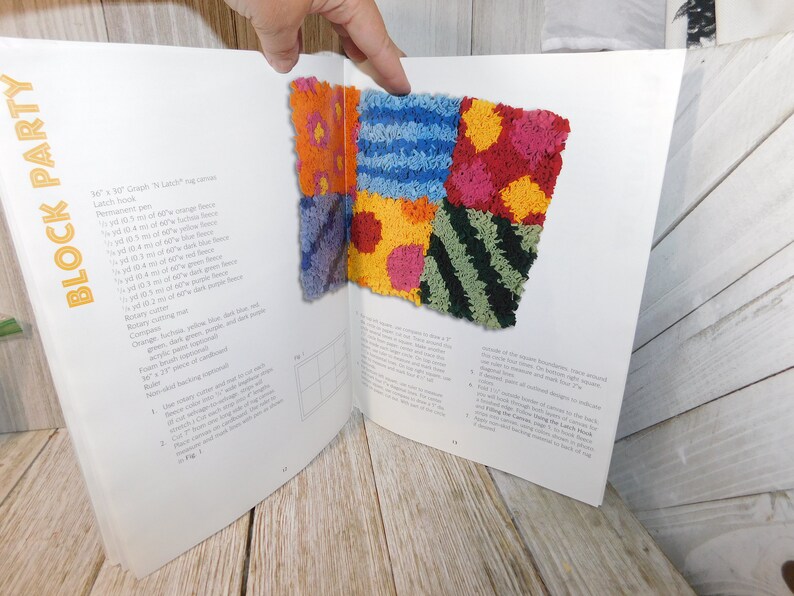 May include: A book open to a page showing instructions for a latch hook rug project. The rug is made of colorful squares of different textures and patterns, including stripes, polka dots, and zigzags. The page also lists the materials needed for the project, including yarn, latch hook, and canvas.