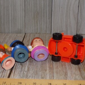 May include: Four plastic figurines and a red toy car. The figurines are of people with different coloured clothes and hair. The car has black wheels and a red body.