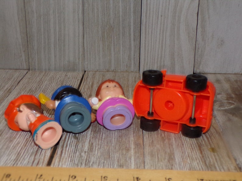 May include: Four plastic figurines and a red toy car. The figurines are of people with different coloured clothes and hair. The car has black wheels and a red body.