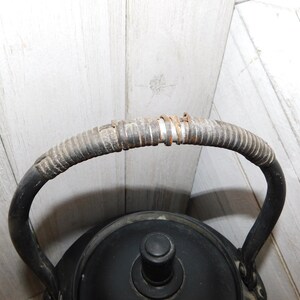 May include: Black cast iron kettle with a woven handle. The kettle has a black lid with a knob on top.