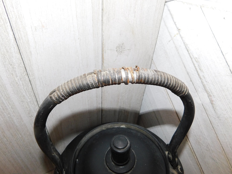 May include: Black cast iron kettle with a woven handle. The kettle has a black lid with a knob on top.